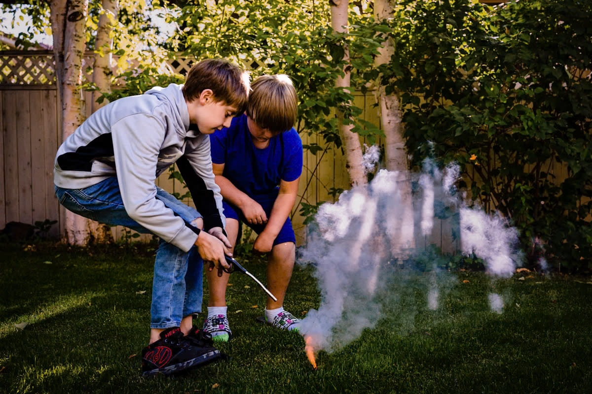documentary photograph of two pre-teen brothers lighting a smoke bomb in their back yard