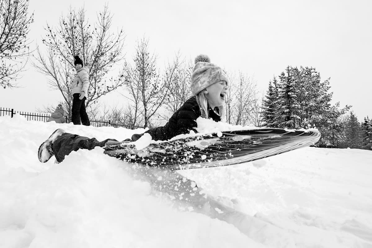 documentary photograph of little girl launching into air on her snow toboggan