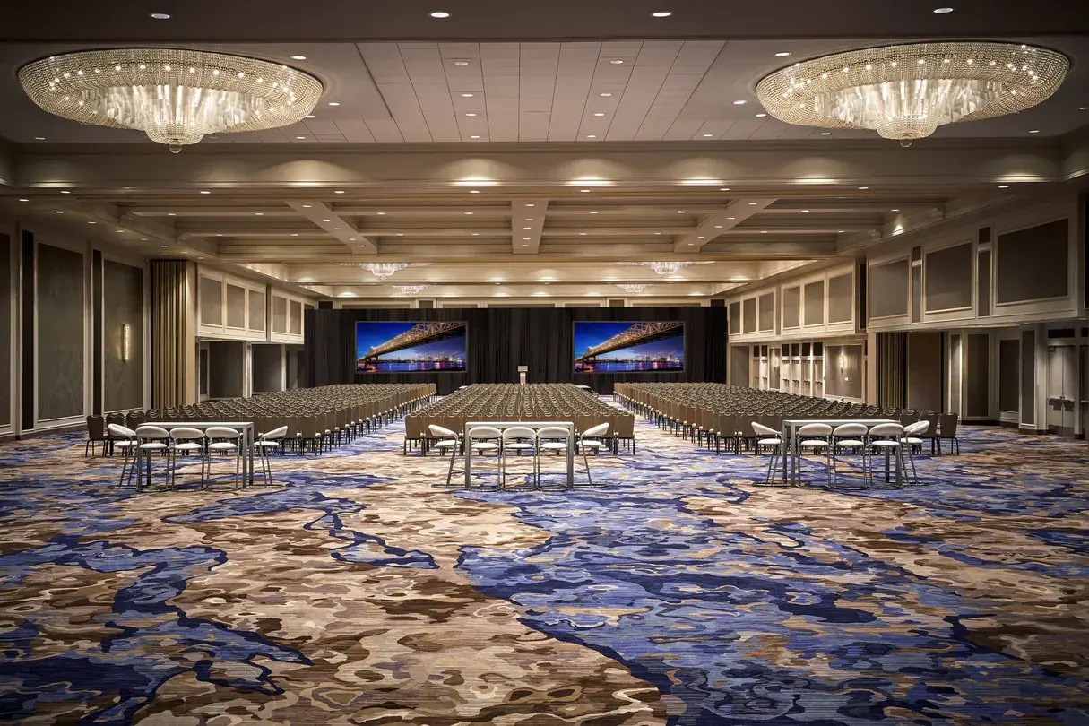 Photo inside New Orleans Marriott: Ballroom shows crystal chandeliers, theater-style seats, & abstract designed blue carpet