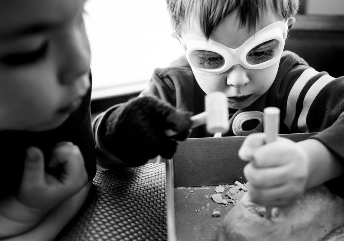 documentary photograph close up of brother with goggles carefully chiselling a rock while little brother looks on