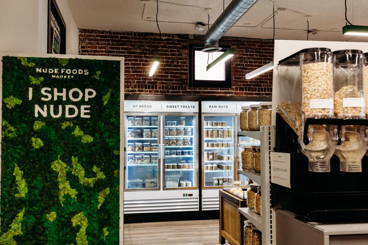 moss wall that says "I shop Nude" inside a zero waste grocery store with bulk dispensers and jars of food