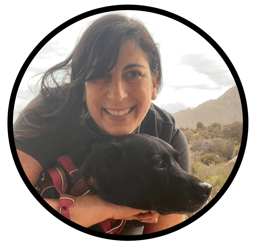 Jill Aronoff smiling outdoors with her black dog, mountain landscape in the background.