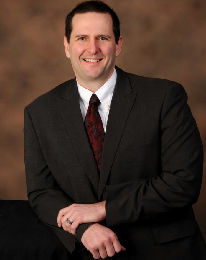 Dr. Wheeler leaning on table and smiling in suit