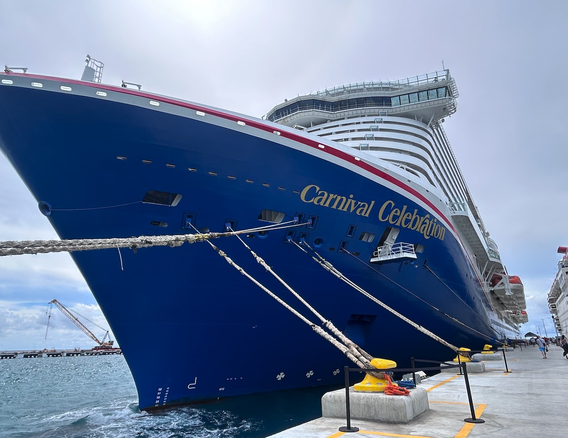 Front of large cruise ship, tied to pier.  Ship is painted blue, with red, white, and gold trim