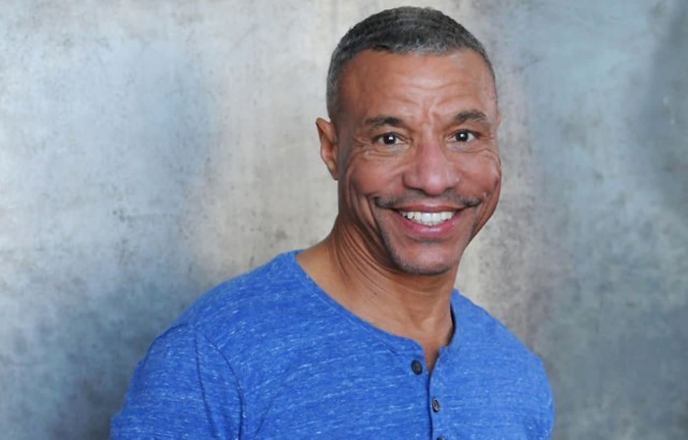 Algiin standing with a broad smile on his face against a blank wall