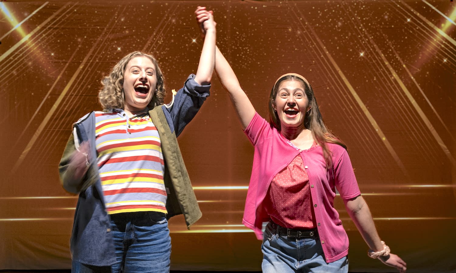 The characters Emma and Alyssa holding hands overhead, celebrating
