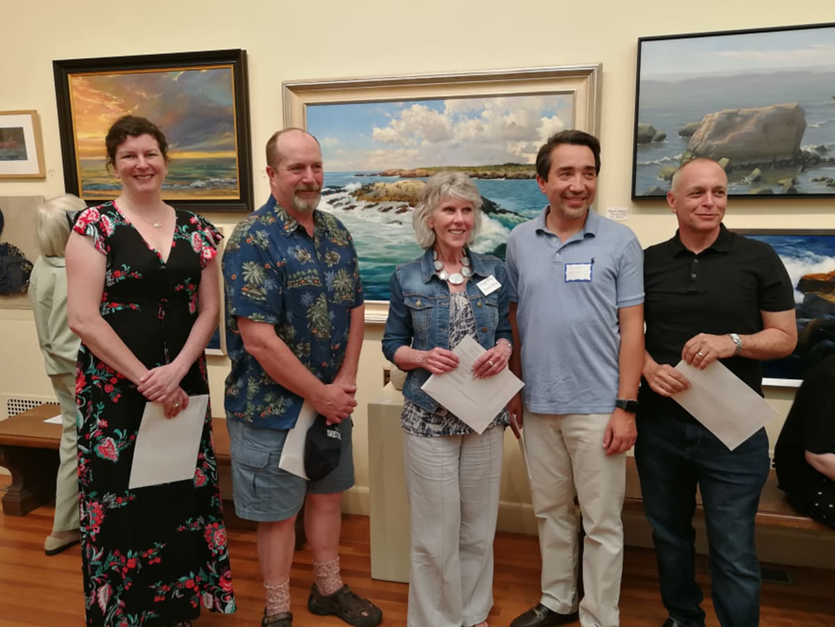 Five people stand in front of paintings