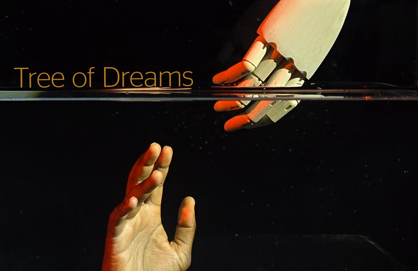 The hand of a wooden puppet or marionette reaches through a watery barrier to reach out to a human hand extended