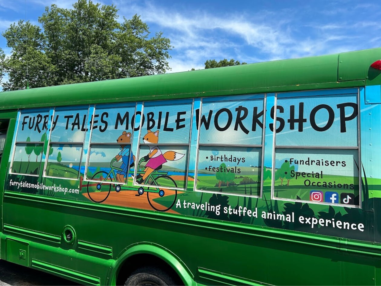 Green Bus with a cartoon image of a bear and a fox riding a tandem bike and the words "Furry Tales Mobile Workshop"