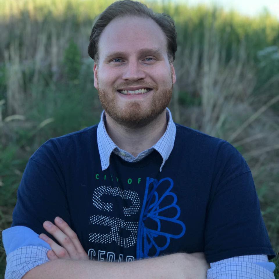 Phillip Platz stands in front of a field of prairie grass wearing a City of Cedar Rapids t-shirt.