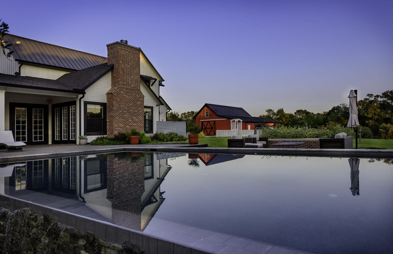 Farmhouse-style pool with brick fireplace and red barn backdrop in Bellville, Texas by Sunset Pools.