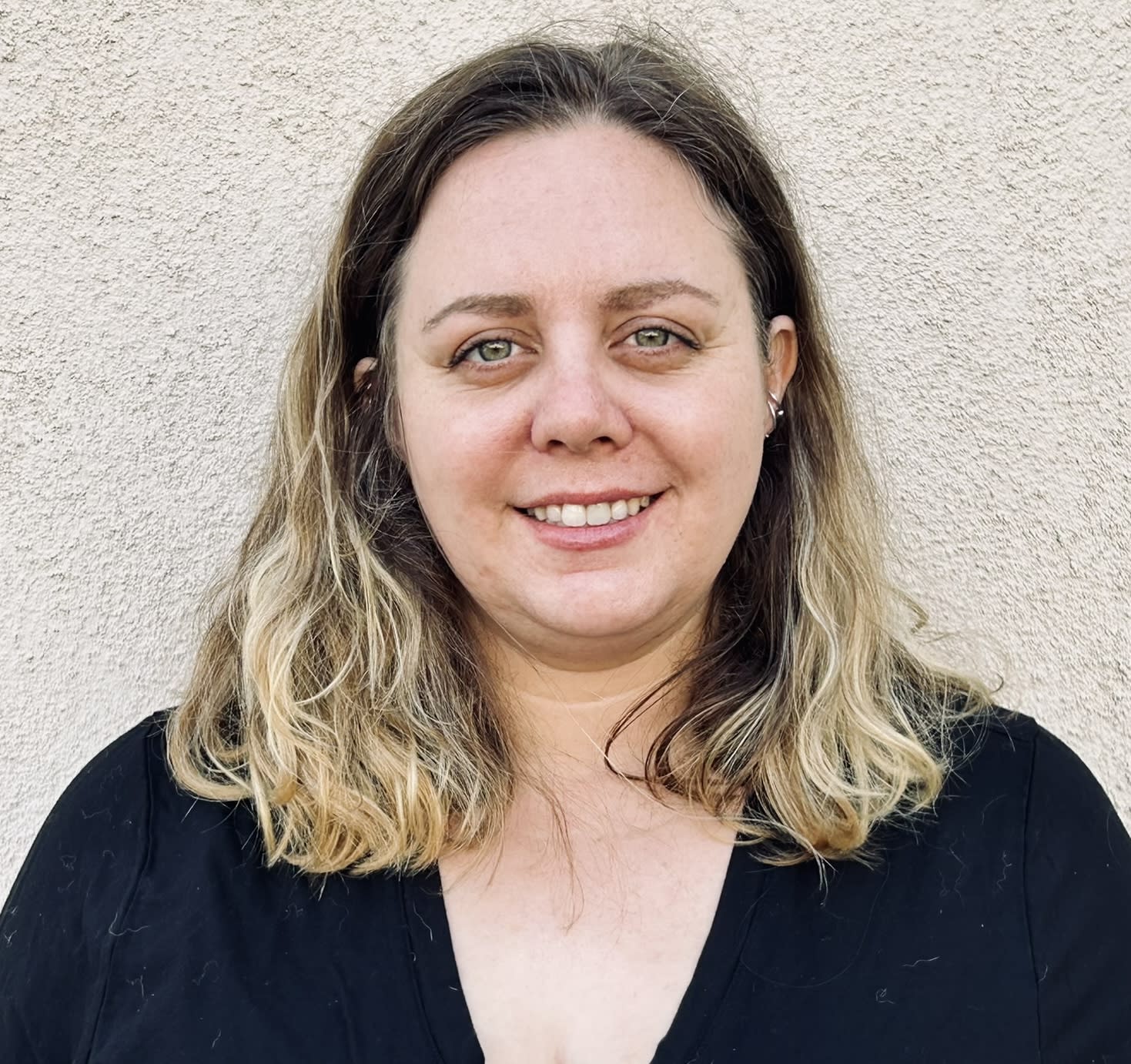 Sabrina has long dark blond hair and is wearing a black v-neck top