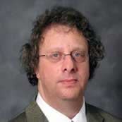 William has curly brown hair and wears wire-framed glasses