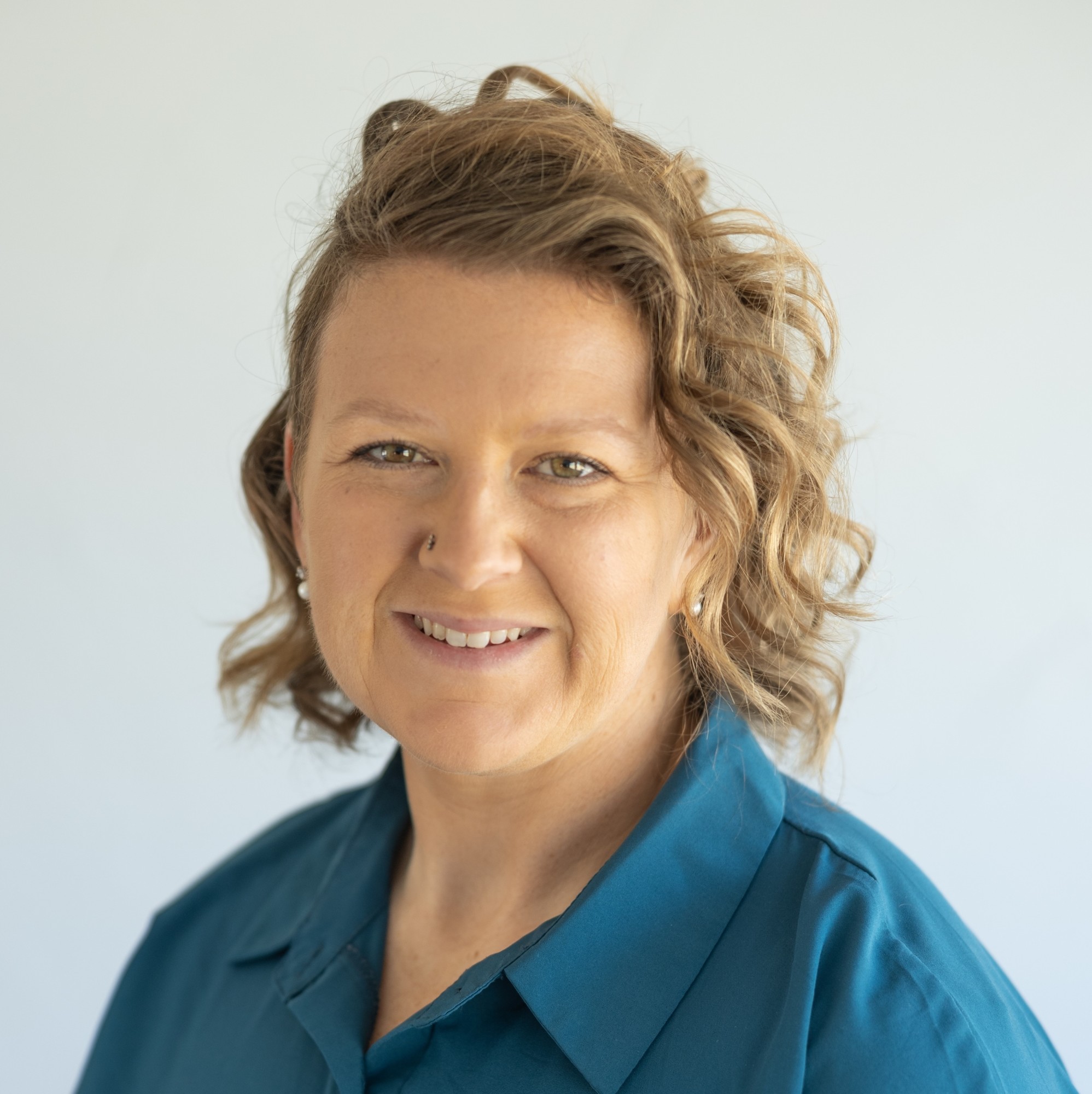 Meghan has short, wavy, blond hair and is wearing a teal button-up shirt