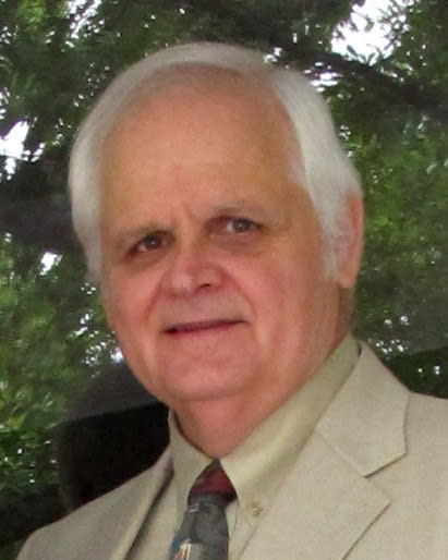 Walter is wearing a light colored suit standing in front of some trees