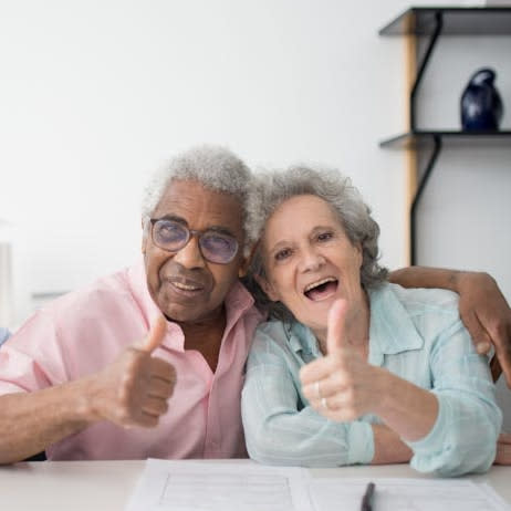 two older adults smiling and giving a thumbs up sign