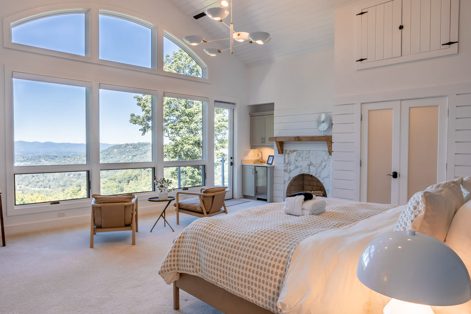 Luxury primary bedroom with vaulted ceilings, oversized picture windows, mountain views, sitting area, and elegant fireplace