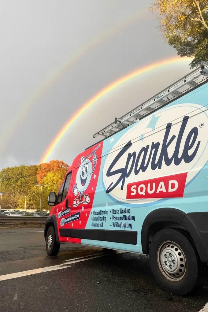 Sparkle Squad cleaning service van parked under a rainbow after rain, showcasing professional window and house washing servic