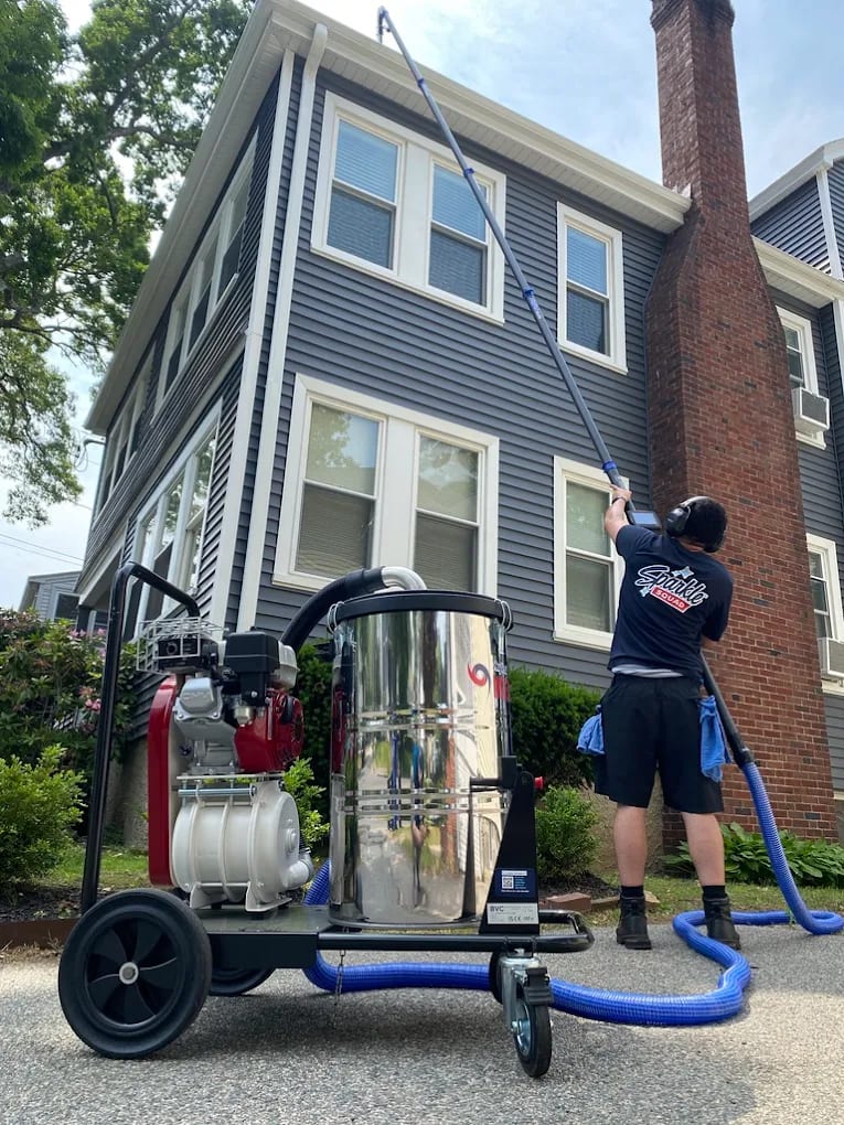 Sparkle Squad technician using professional vacuum equipment to clean second-story gutters on a residential home.