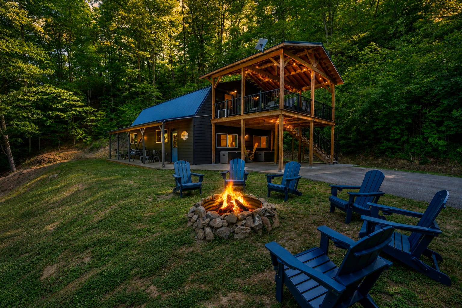 Modern mountain cabin at dusk with a glowing fire pit, Adirondack chairs, covered upper deck, and peaceful forest surrounding