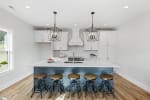 Modern kitchen by Heroic Builders featuring white cabinetry, a blue island with seating for five, and quartz countertops