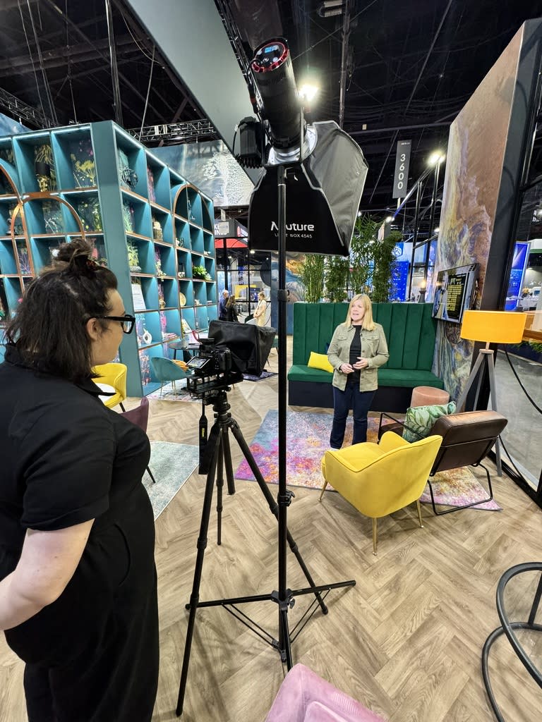 Camera operator filming a woman on a set with studio lighting at a trade show booth.