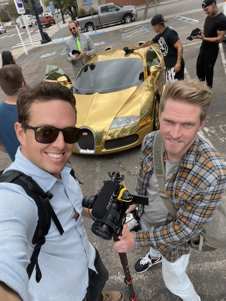 Camera operators posing for a selfie next to a gold luxury sports car.