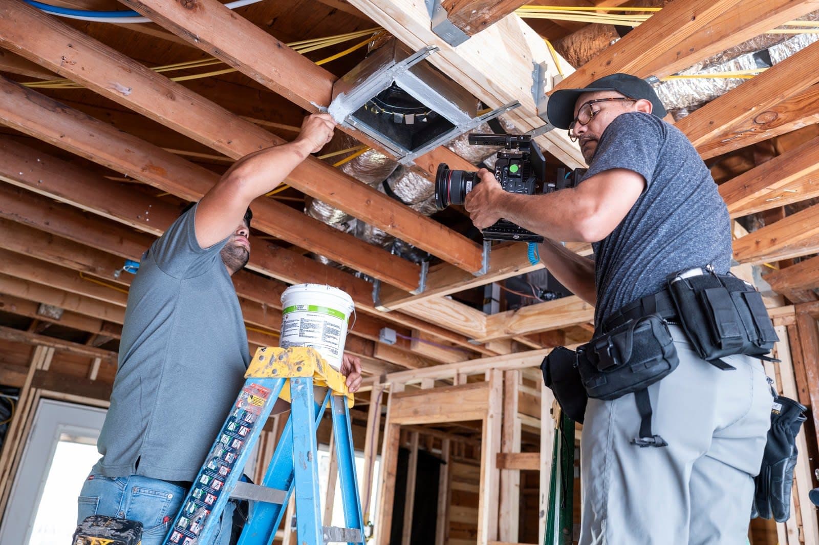 A camera operator films a contractor on a ladder inside a house being rebuilt for the City of San Antonio.