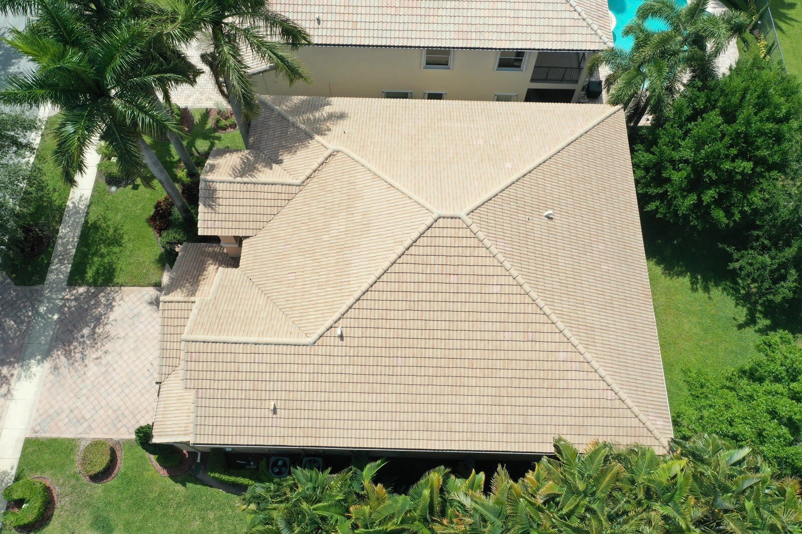 Drone view of a sand-colored tile roof on a single-story home with palms in Boynton Beach