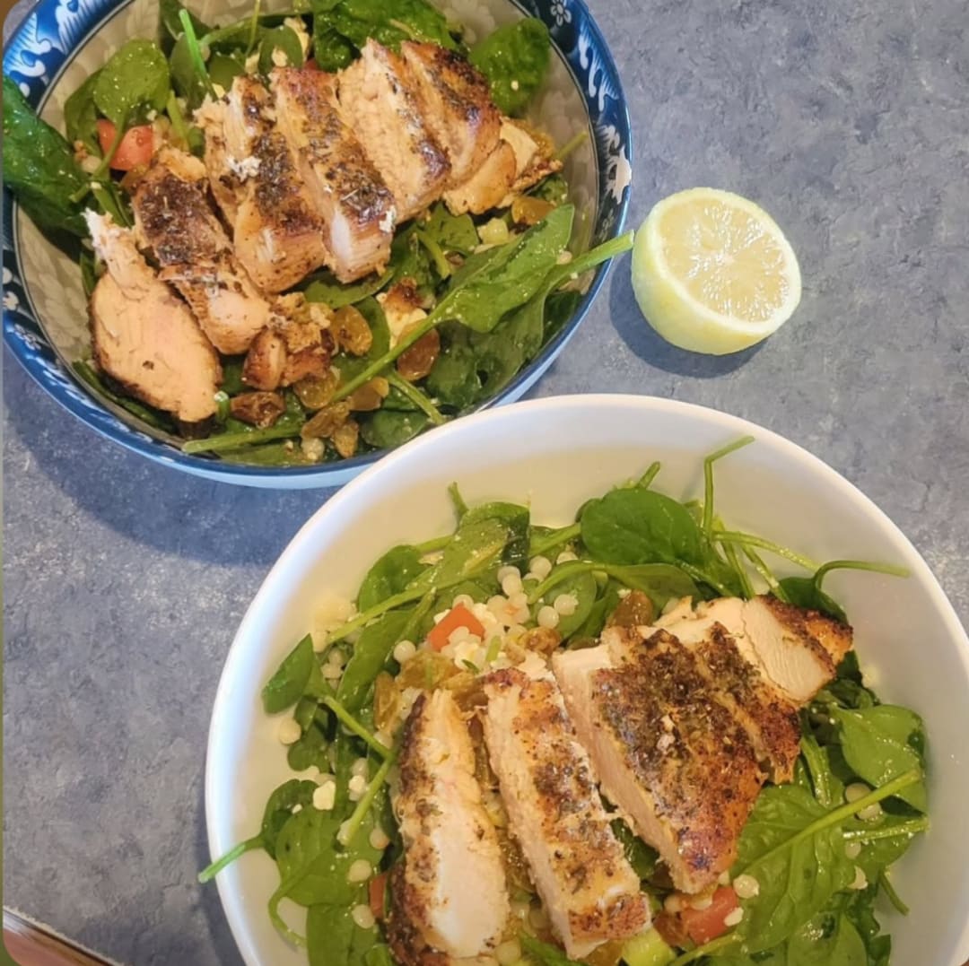 Bowls of grilled chicken salad with spinach, vegetables, and lemon