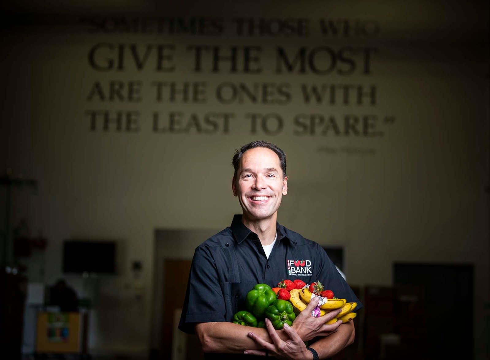 Eric Cooper of the San Antonio Food Bank holds an armful of fresh produce in front of a quote painted on the wall.