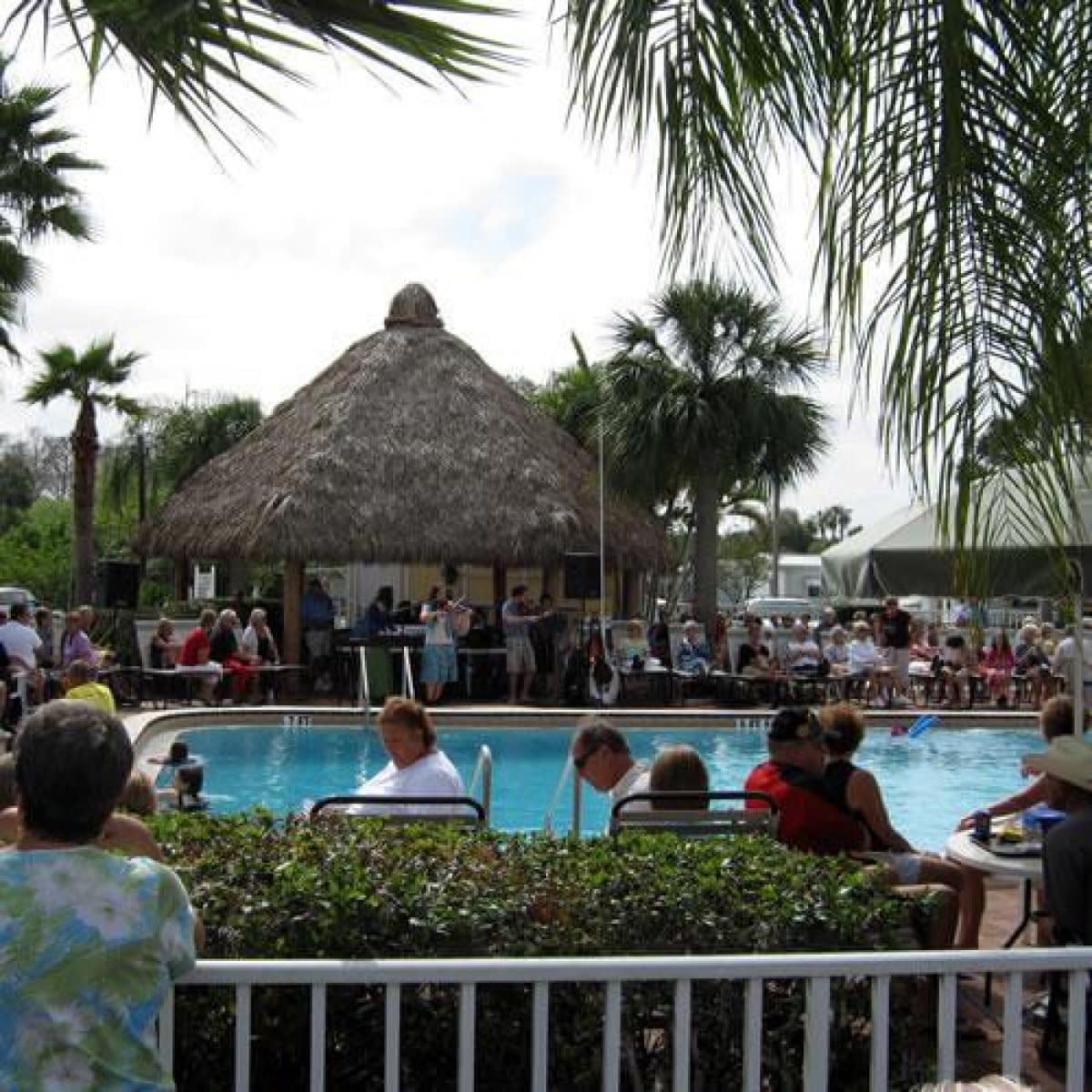 Poolside concert with crowd gathered around thatched-roof tiki hut