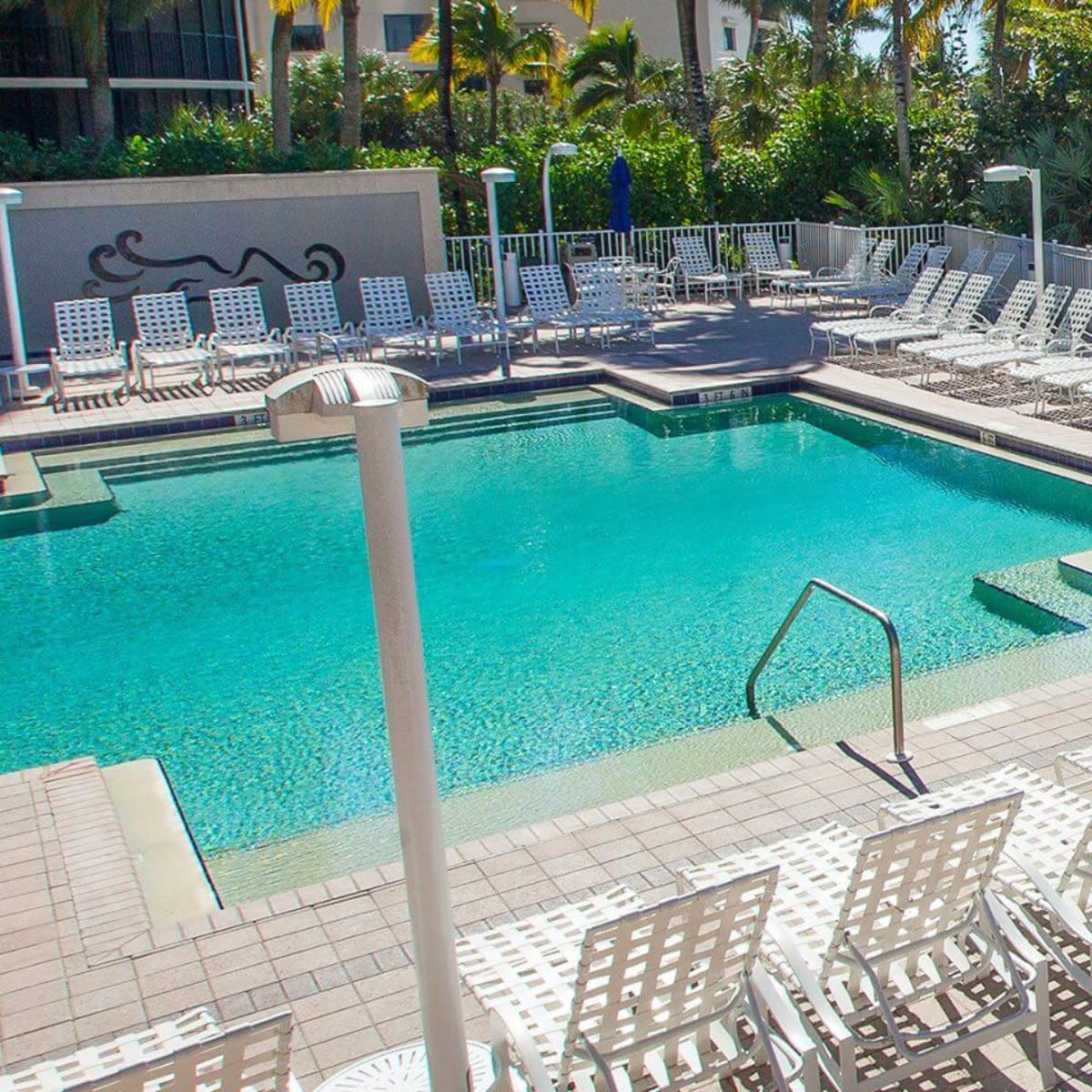 Outdoor swimming pool with white lounge chairs, umbrellas and palm trees
