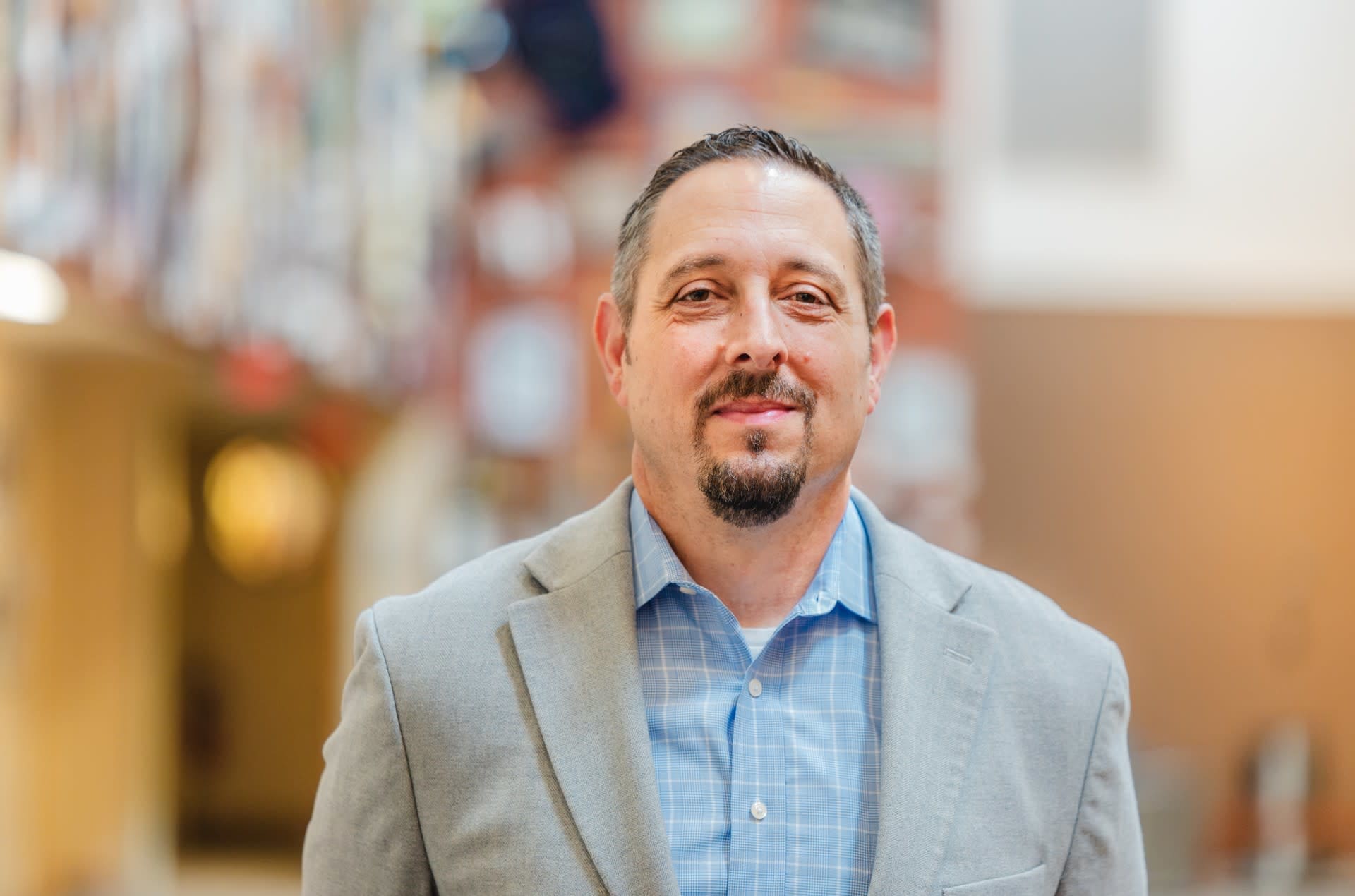 A man with a moustache and beard in a blue shirt and gray jacket