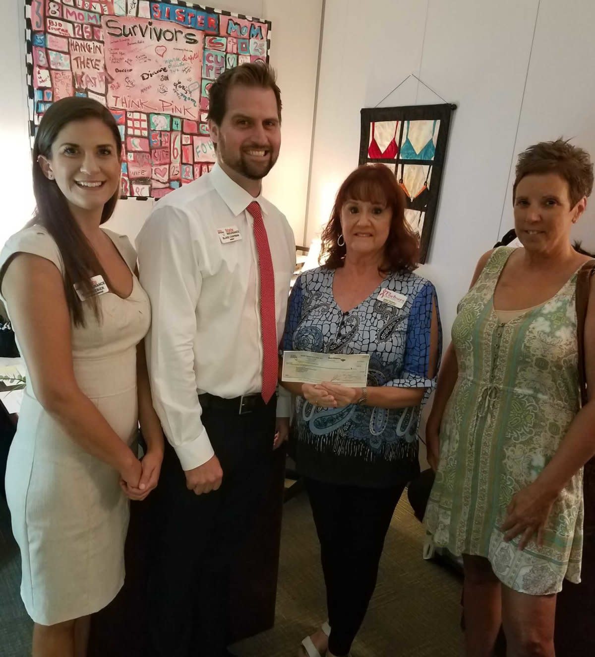 Four adults presenting check at nonprofit event, colorful survivor artwork displayed on wall behind.