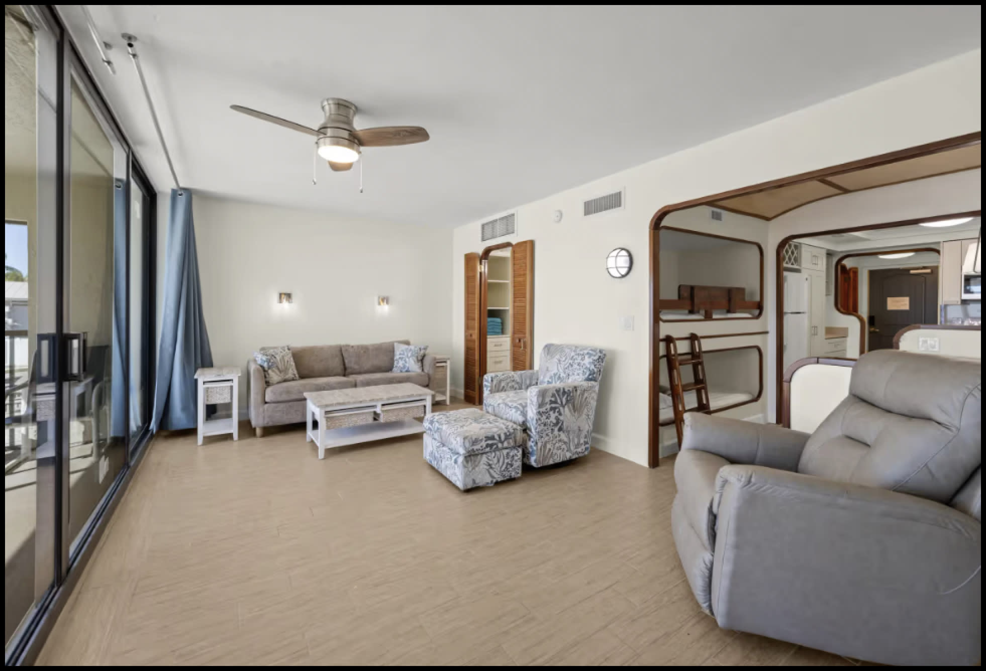 Sunny living room with gray seating, sliding doors, and view into bunk area.