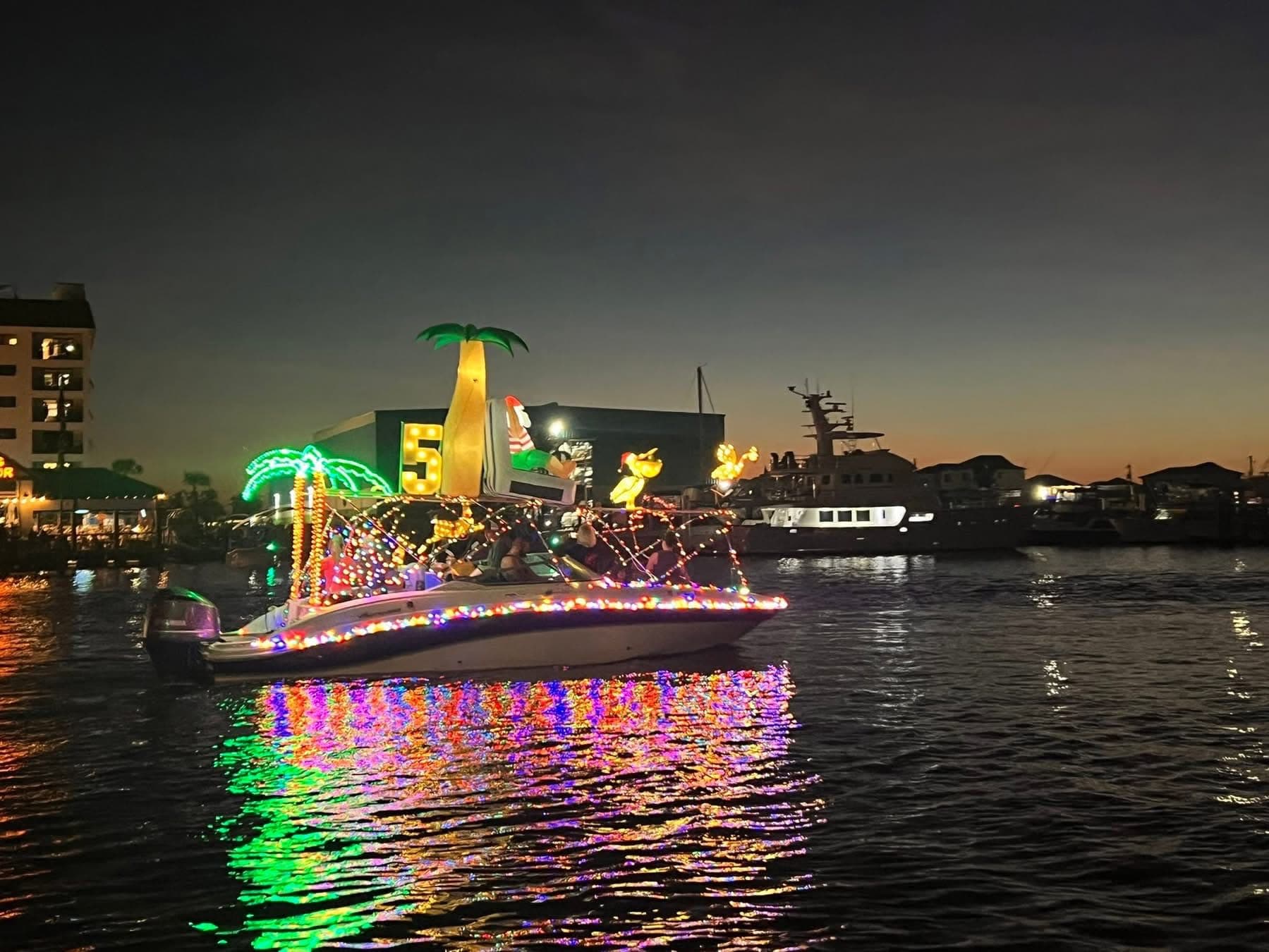 Boat wrapped in lights with glowing palm trees, reflected on dark water