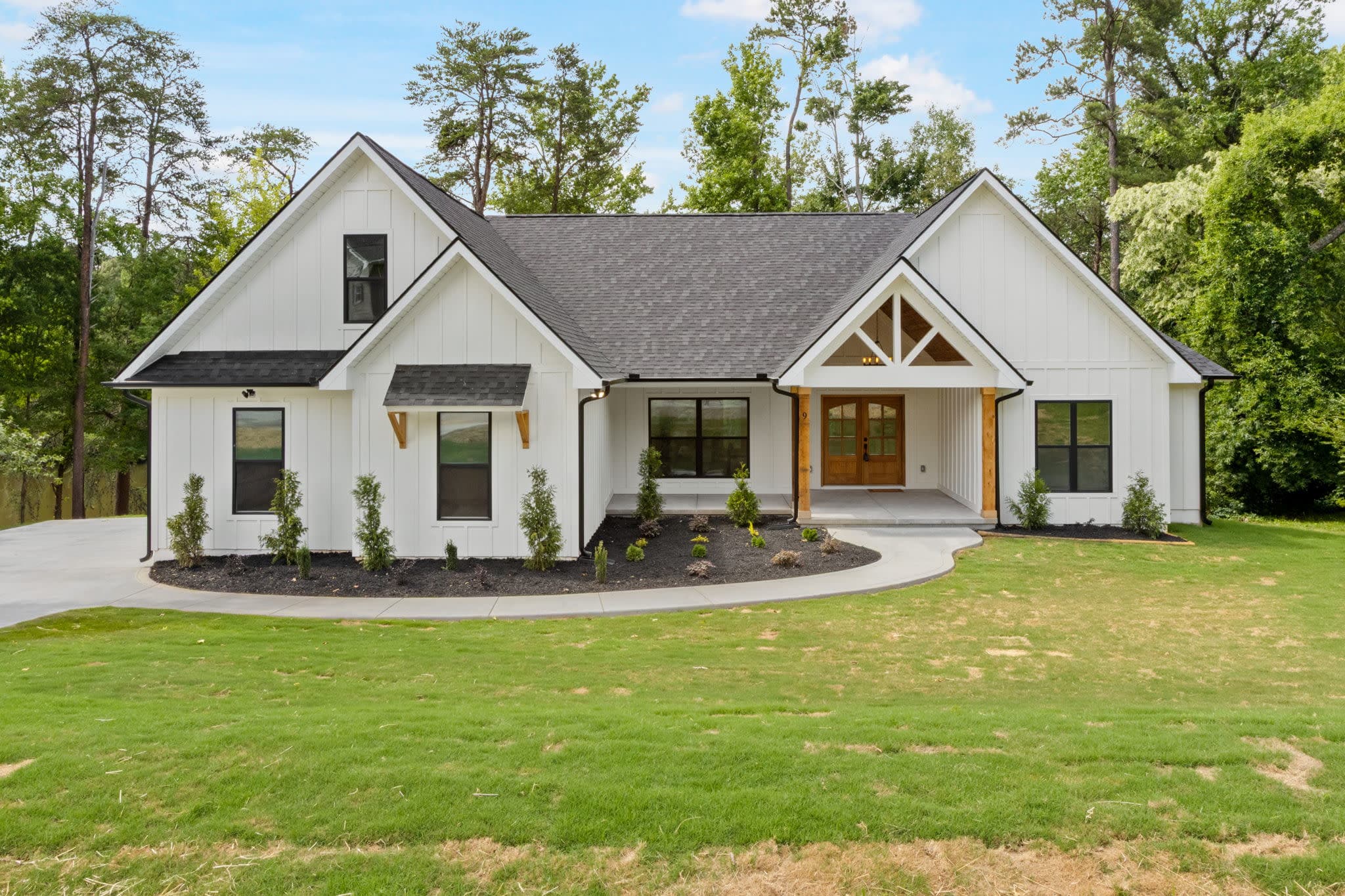 Custom new construction home by Heroic Builders featuring white board and batten siding, black windows, a covered front porch