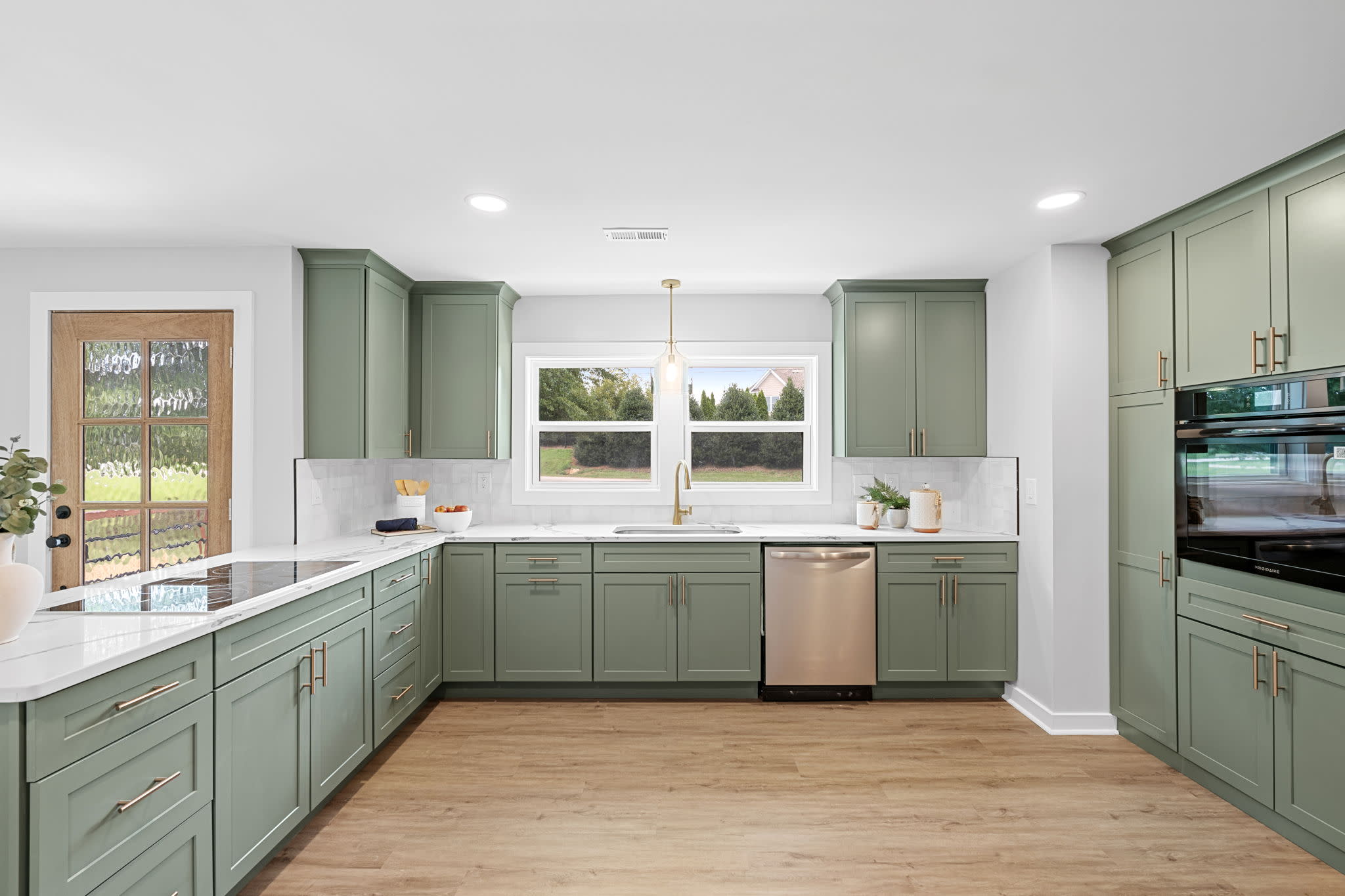 Custom kitchen featuring sage green cabinetry, white countertops, stainless steel appliances, and natural wood flooring.