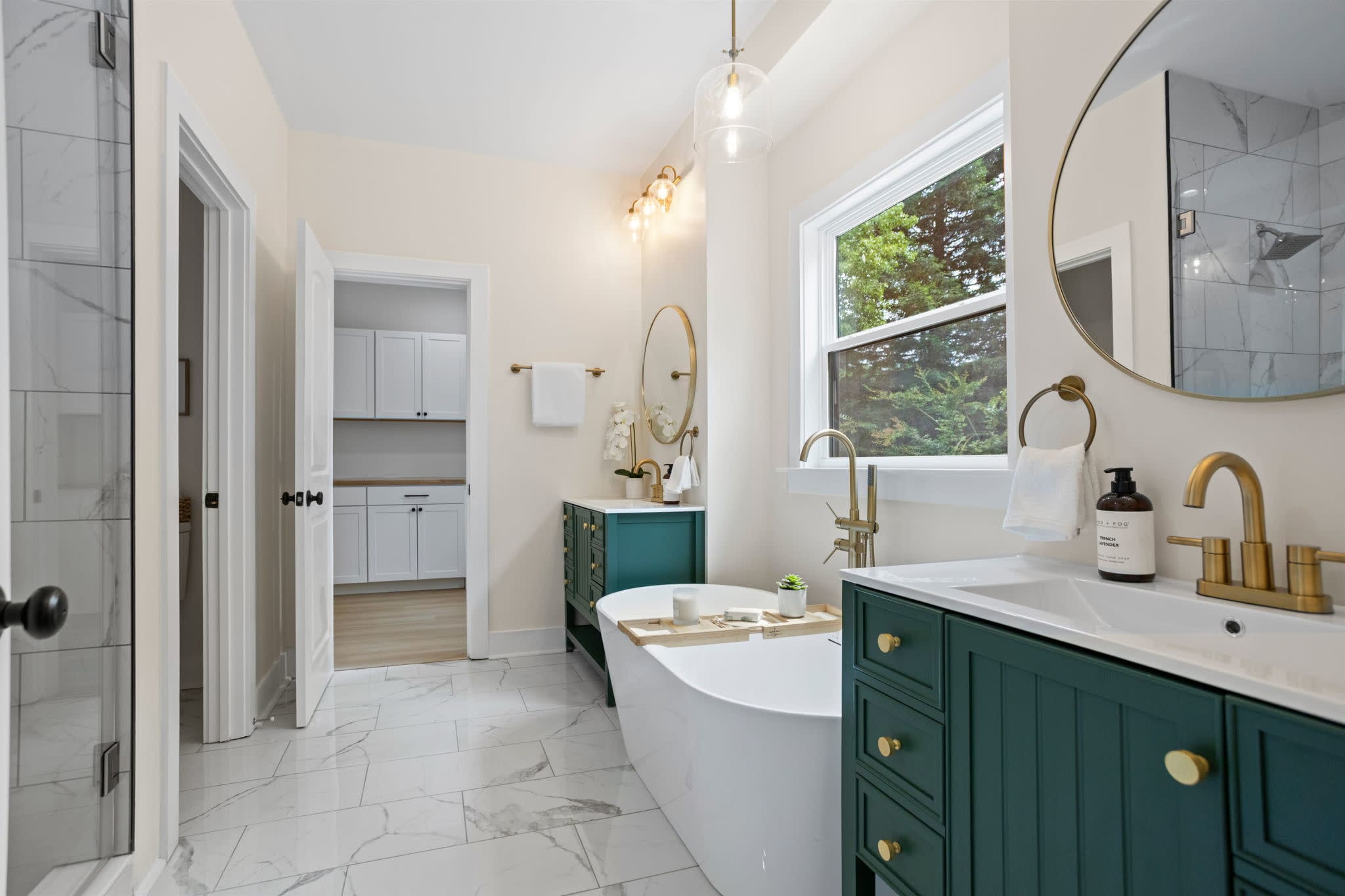 Modern bathroom featuring a double sink vanity, marble look countertops, round mirrors, and a glass enclosed tile shower.