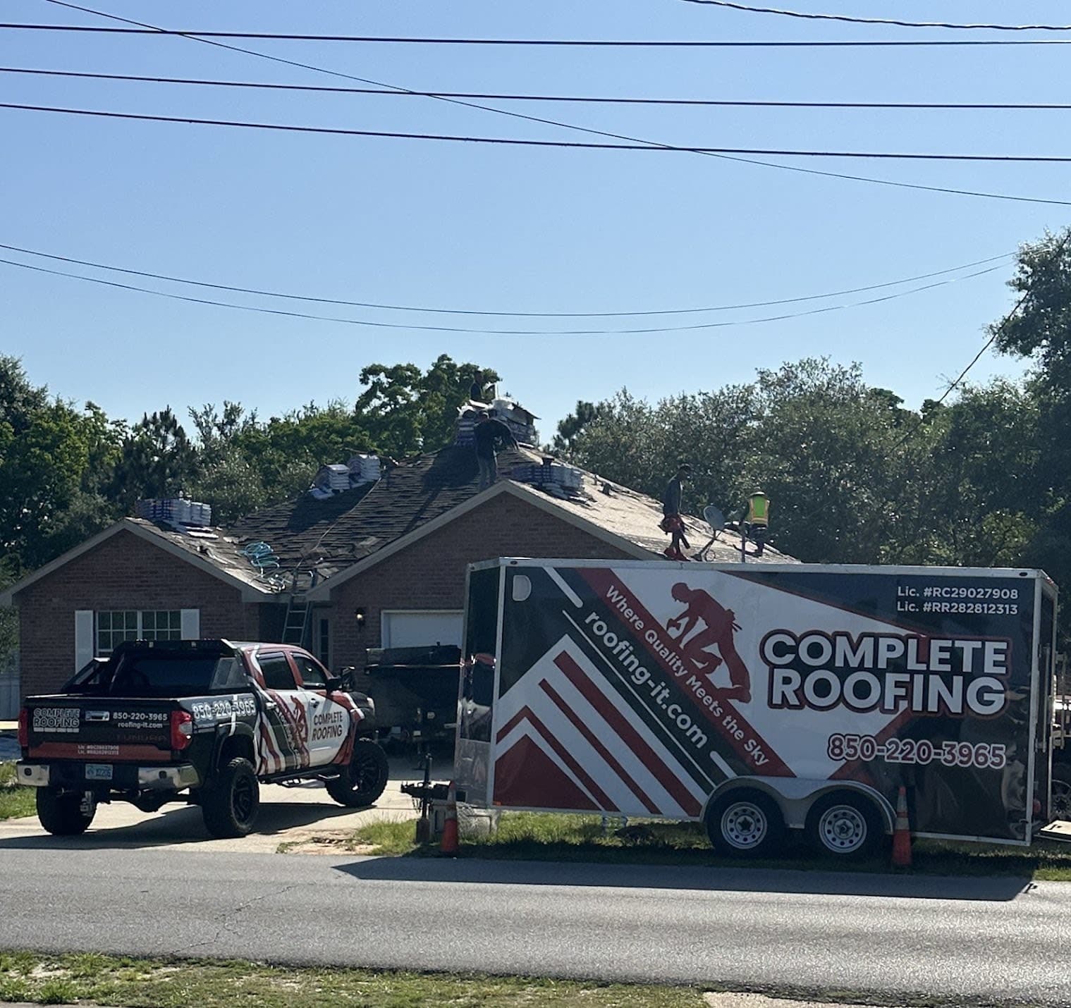 Complete Roofing crew replacing the roof of a brick home in Navarre, Santa Rosa County, Florida, with the company's branded t