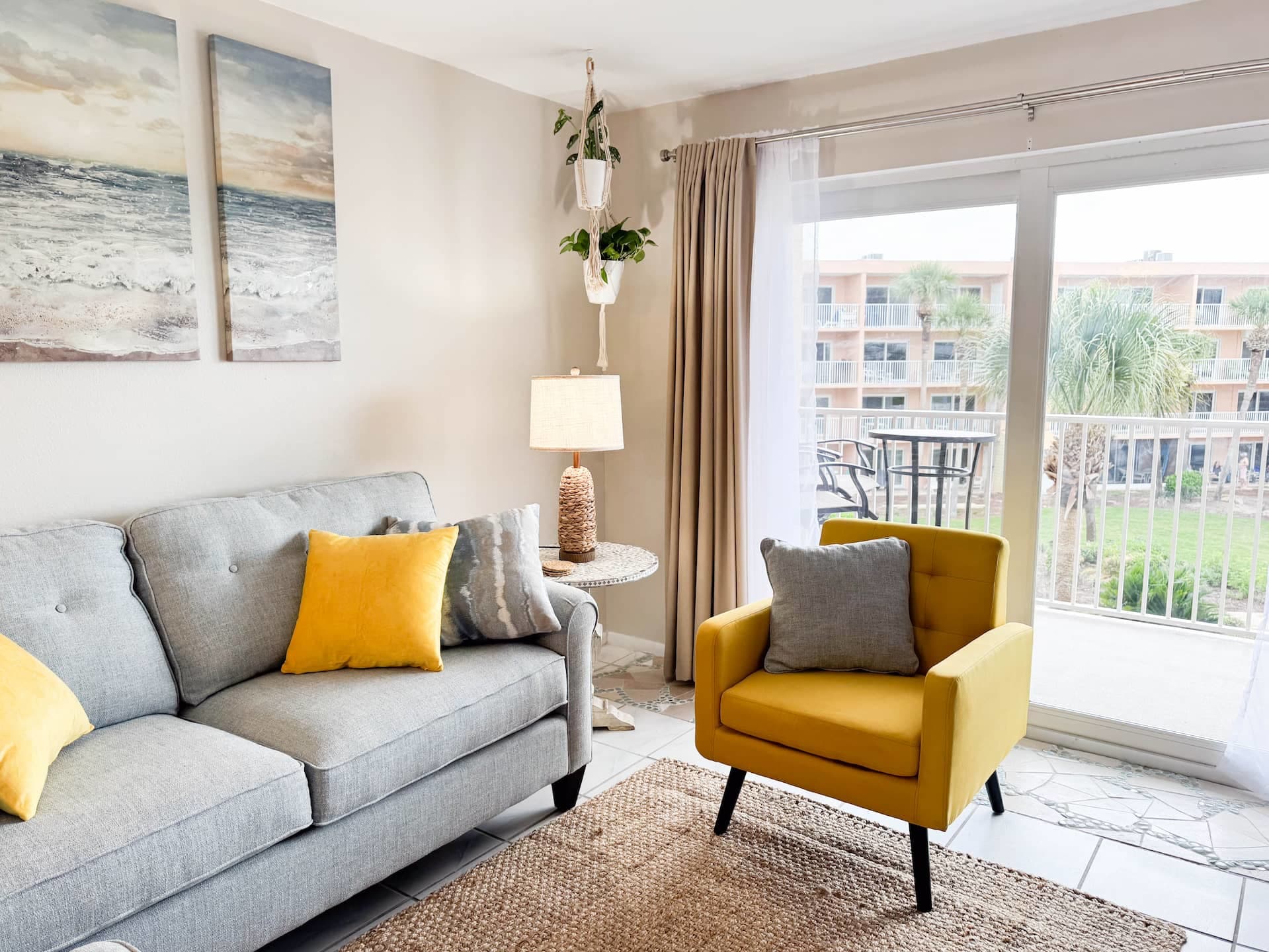 Bright living room with a gray sofa, yellow accent chair, and sliding doors to the balcony at Coastal Dreams.