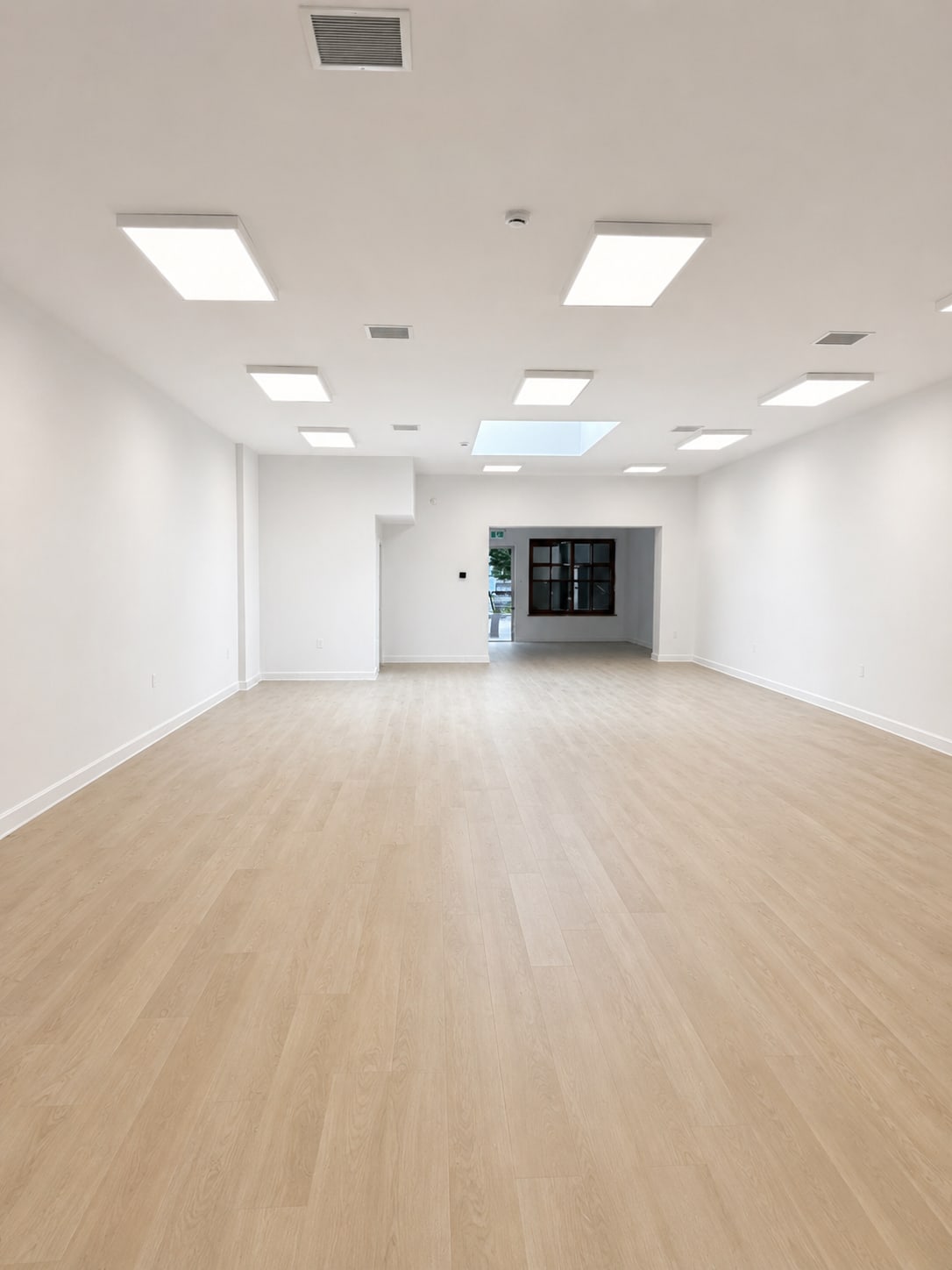 Large renovated commercial interior at 5559 West 8th Blvd featuring light wood flooring, bright white walls, upgraded lightin