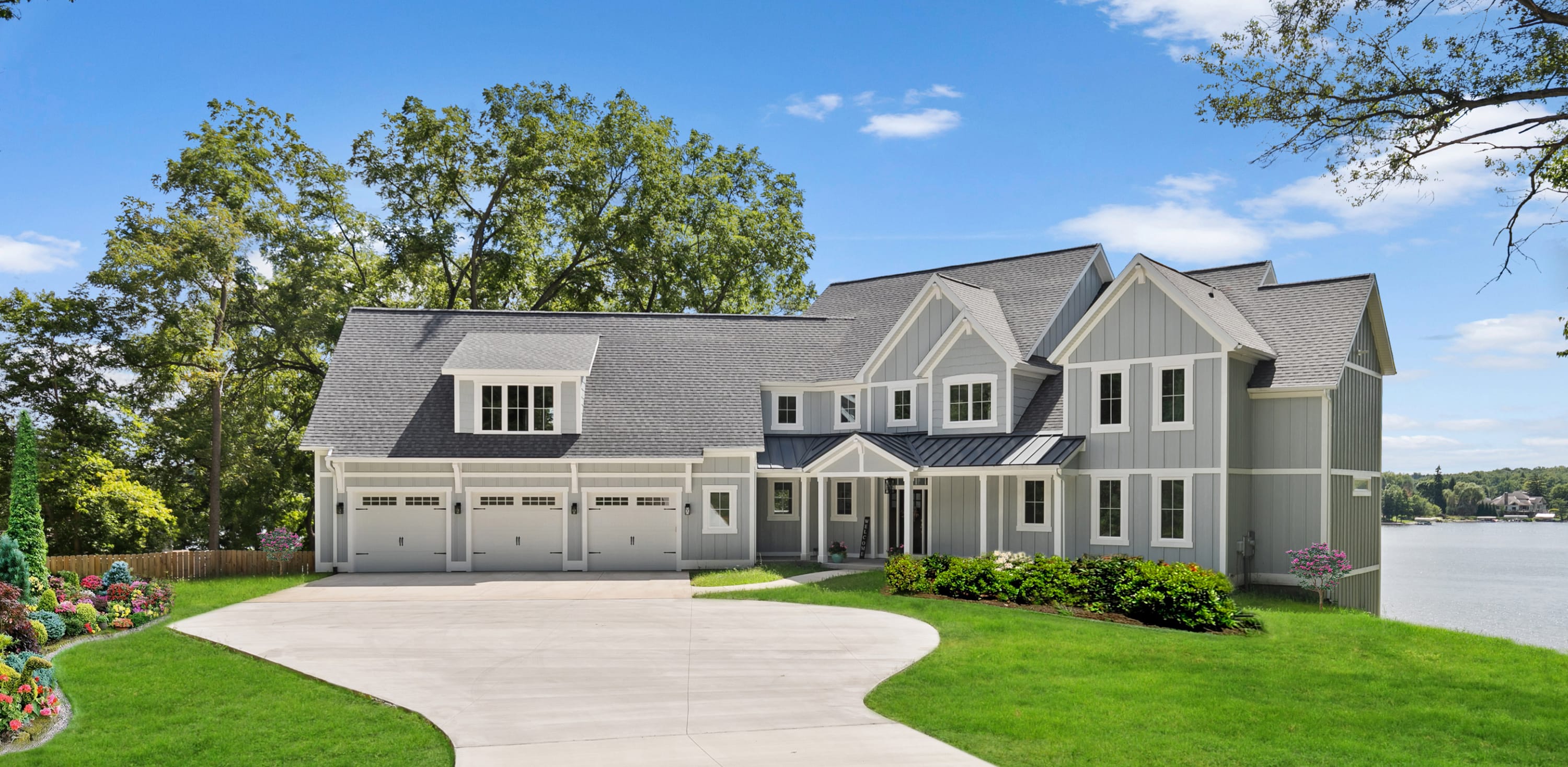Custom lakefront home with gray siding, three-car garage, and curved driveway, built by Spaces Designer Homes in West Michiga