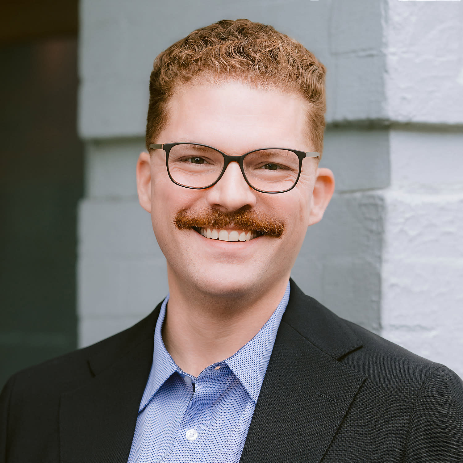 An auburn-haired man wearing glasses and a suit without a tie.