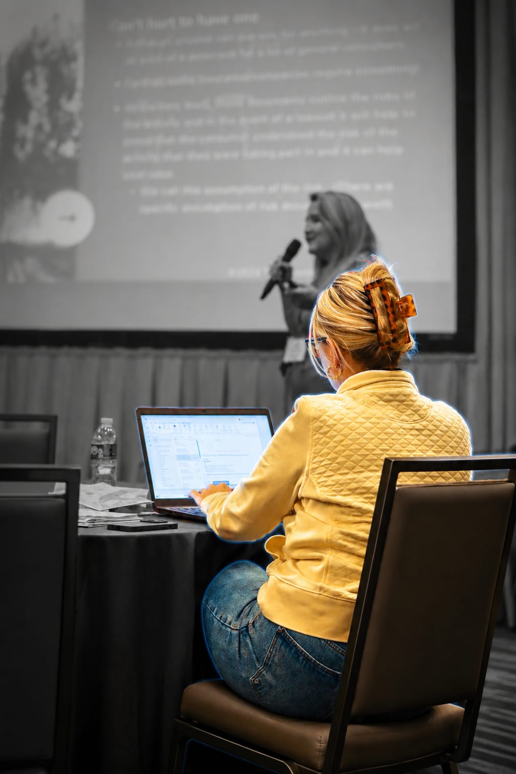 woman uses laptop while speaker presents at conference