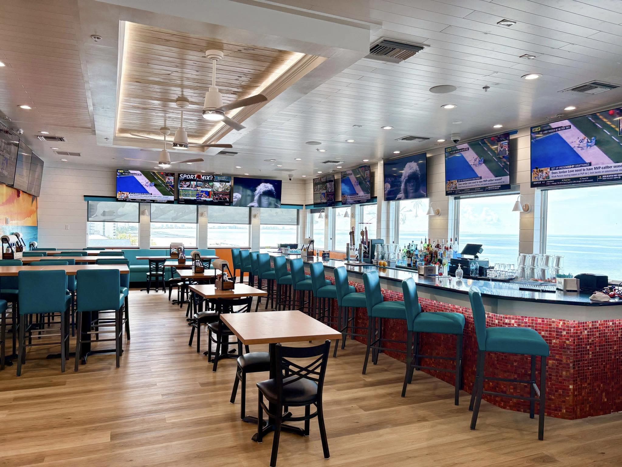 Island View Sports Bar interior with teal seating, TVs, red mosaic bar, and ocean views.
