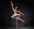 A ballerina in a pink tutu and crown poses en pointe holding up a wooden nutcracker