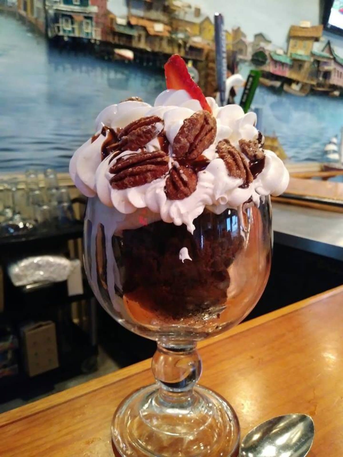 Chocolate dessert in glass topped with whipped cream and pecan halves at waterfront restaurant.