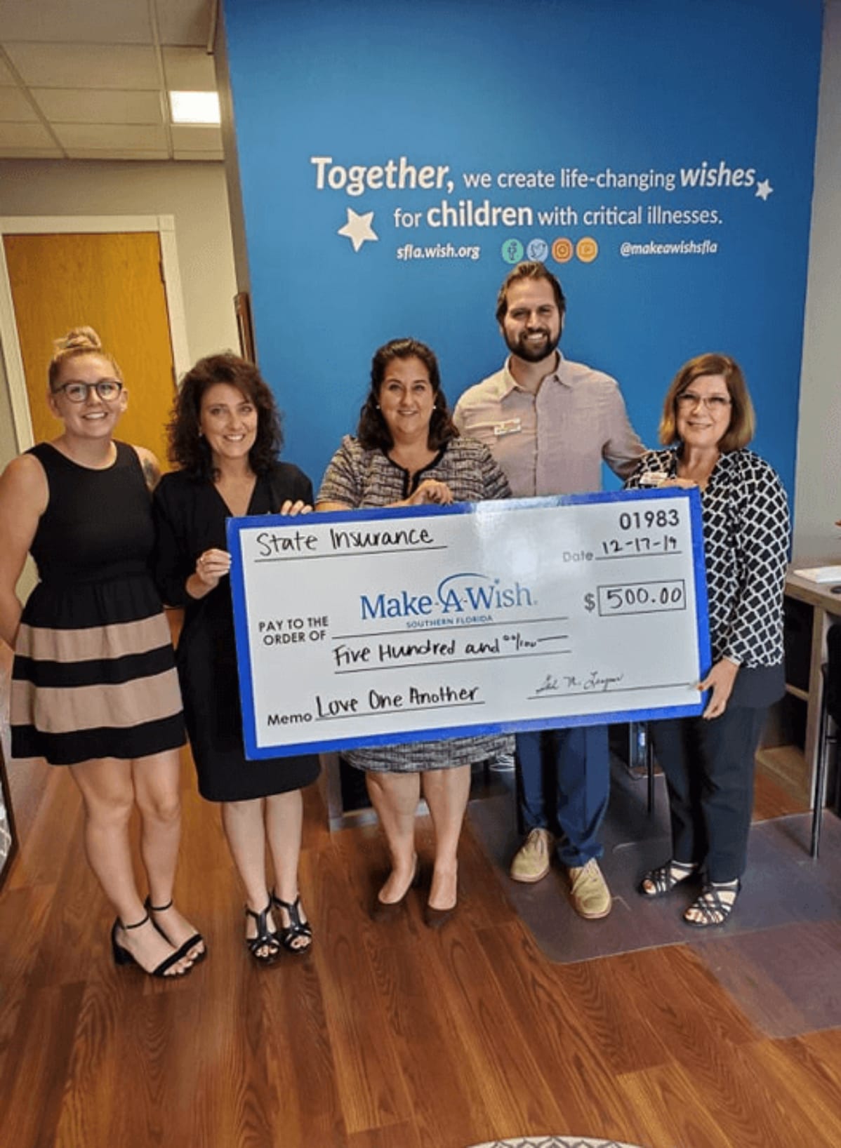 Five people holding large $500 Make-A-Wish check, blue backdrop with organization logo and slogan.